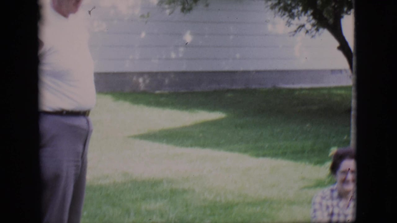 Partial man standing near a lawn with a seated woman visible at the edge of the frame.