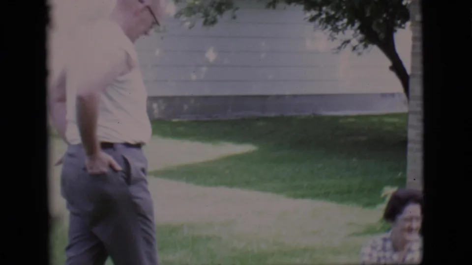A man in a white shirt stands with hands on hips near a walkway and seated woman in this Clarkdale, Arizona 1966 yard scene.