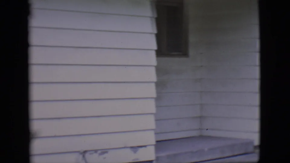 The final frame holds on the Clarkdale house exterior and porch area after the man with the camera has moved out of view.