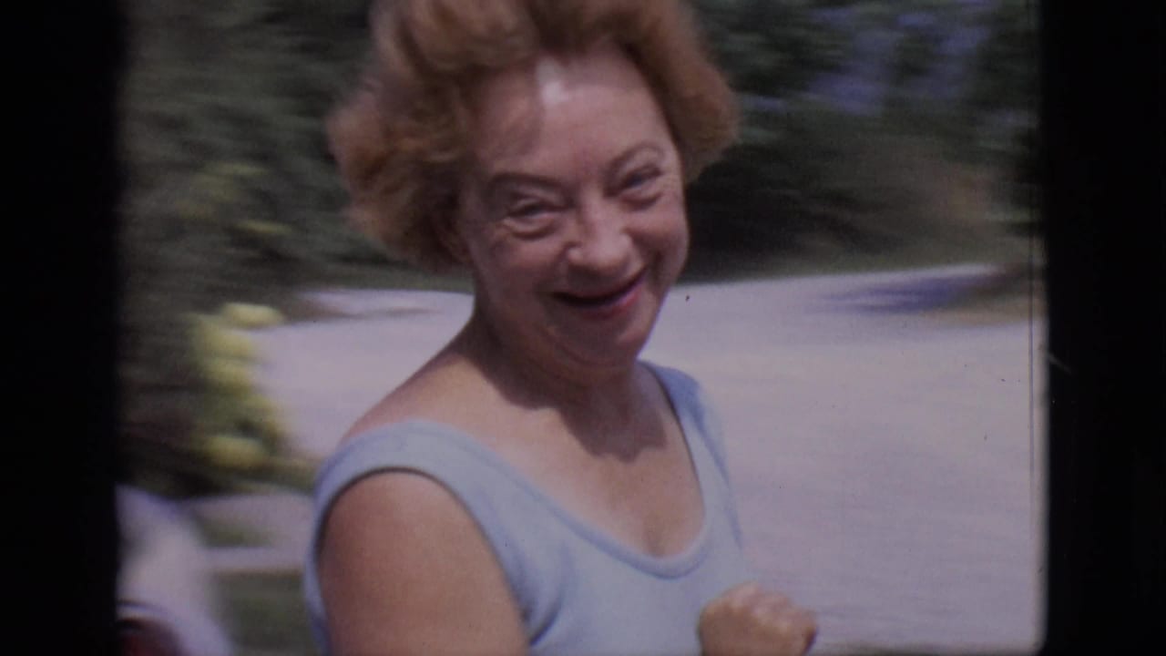 Smiling woman in a light blue sleeveless top moves past the camera outdoors.