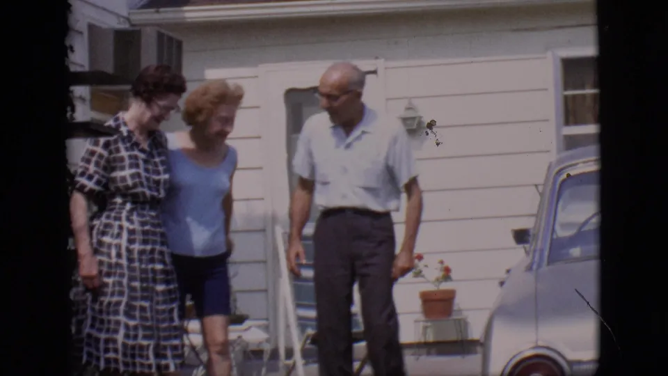 The group shifts position outside the white-sided house in 1966 Clarkdale, with the parked silver car partly visible.