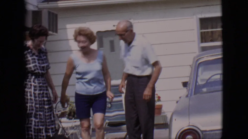 The three adults settle near the residence and parked car, framed by 8mm home-movie gate edges.