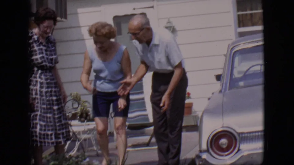 In 1966 Clarkdale, Arizona home-movie footage, three adults gather outside a house near a parked car and look toward a small dog.
