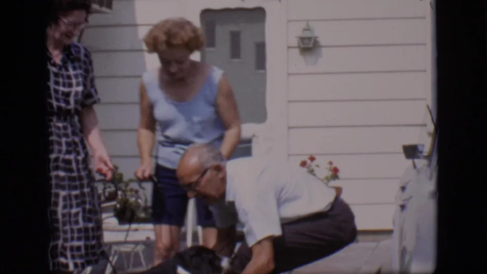 The man crouches to reach the small black-and-white dog as two women watch outside the Clarkdale house.