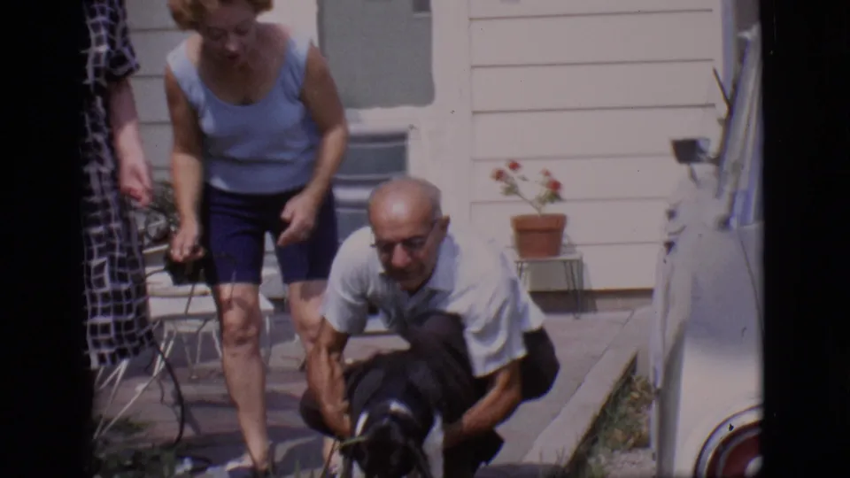 At the end of the clip, the man crouches with the small dog near the porch as the women remain nearby in the 1966 home movie.