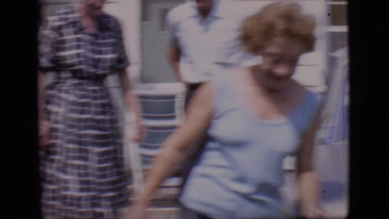 Blurred woman in blue moves past two adults outside a white house.