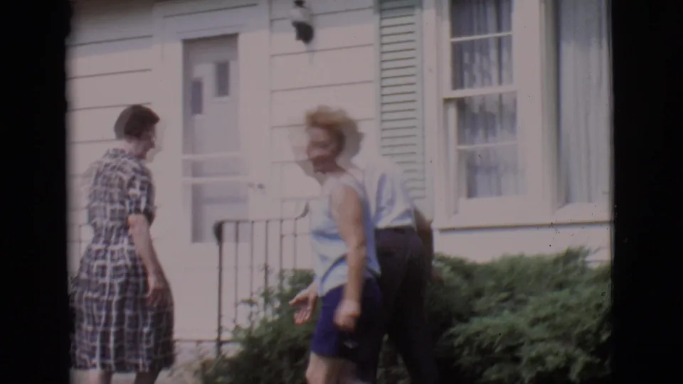 Three adults move casually in front of a white house entrance and bushes in the 1966 Clarkdale home-movie scene.