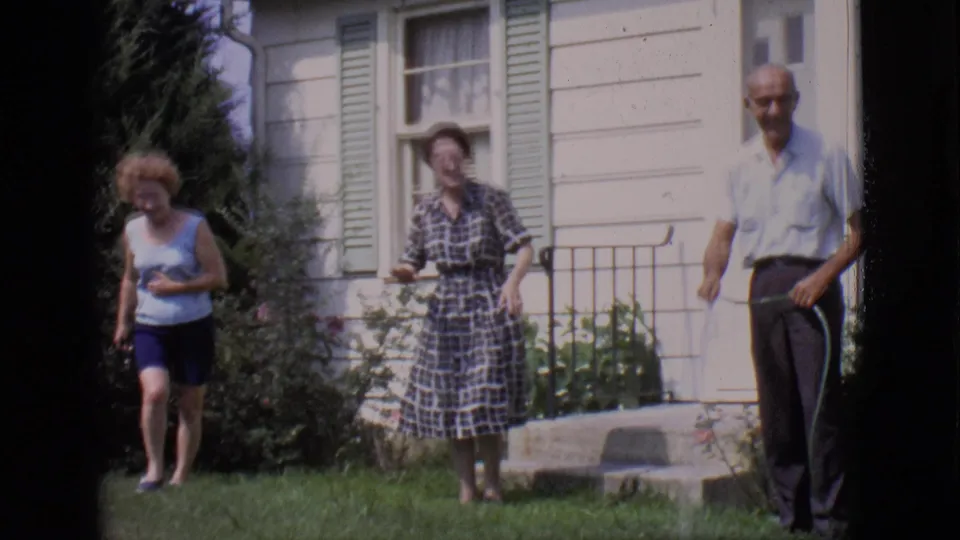 One woman walks across the lawn as the woman in plaid and the older man with the hose remain by the white house in the 1966 scene.