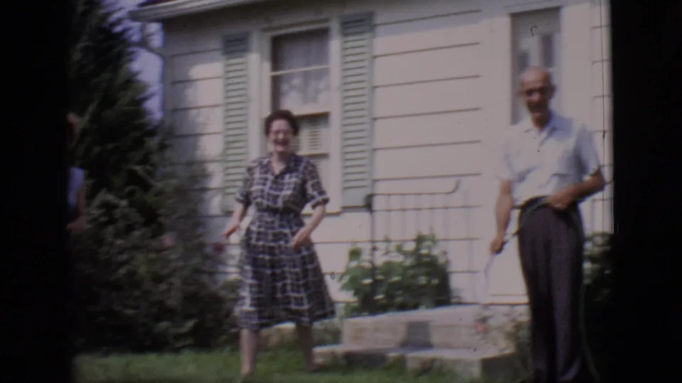 A 1966 Clarkdale backyard moment shows a plaid-dress woman and a man holding a hose beside a house with shutters.