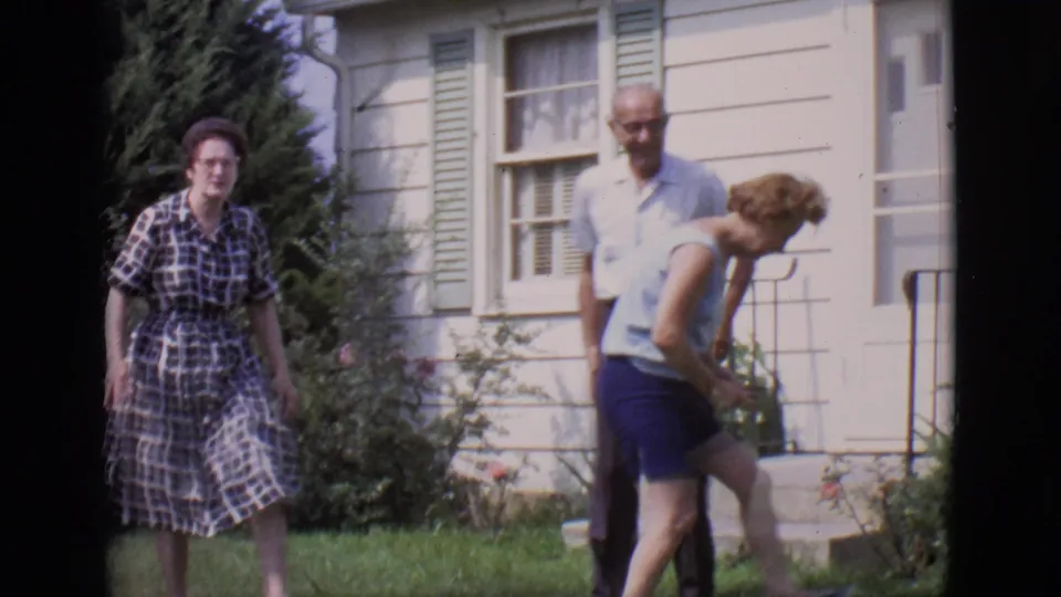 A woman in a plaid dress walks toward the camera as a man and another woman stand near the doorway of the Clarkdale backyard house.