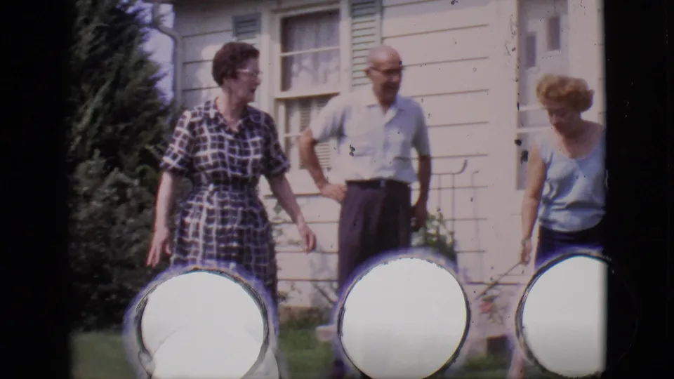 Three adults pause together on the Clarkdale backyard lawn near the house, with visible circular film or reel artifacts along the lower frame.