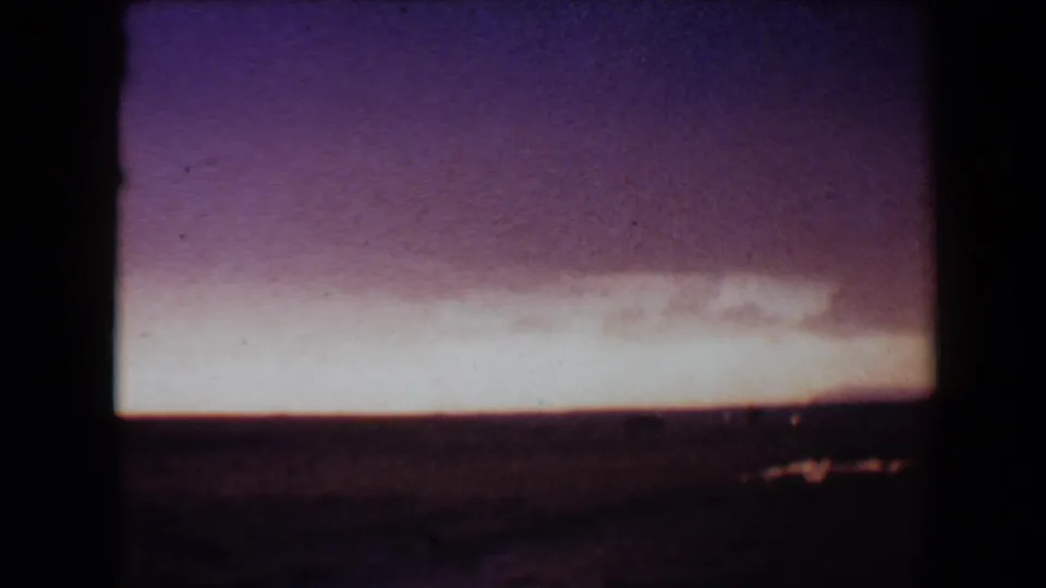1967 Flagstaff home-movie still showing a bright twilight strip, dark lower landscape, and magenta-purple sky on grainy 8mm film.