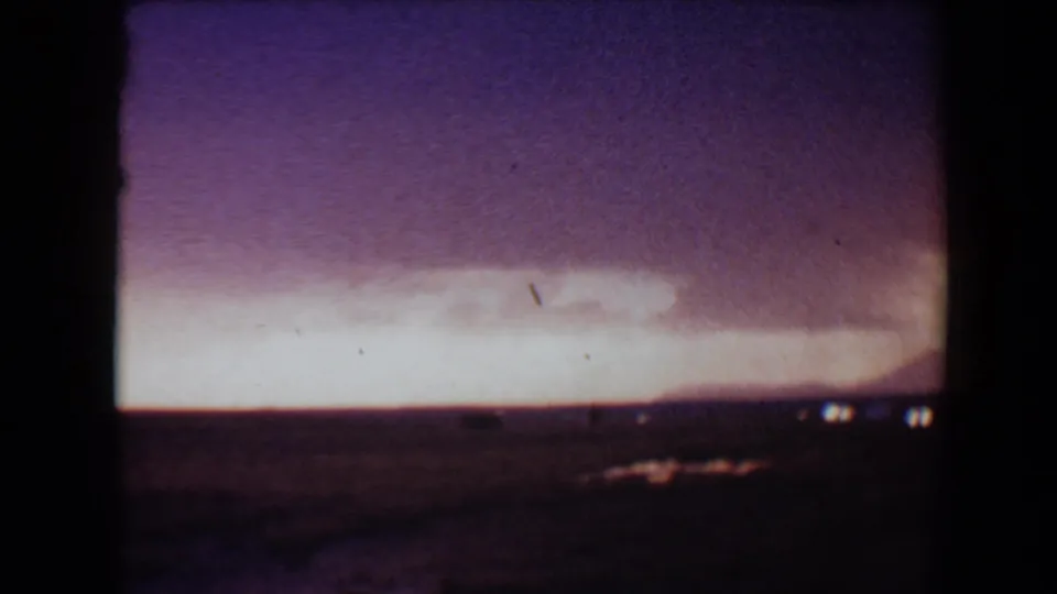 8mm home-movie frame from Flagstaff at dusk, with a pale glow near the horizon and a dark foreground carrying small bright specks.