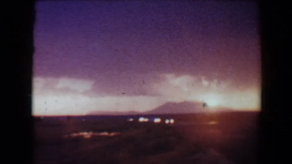 1967 Flagstaff-area 8mm frame with the sun flaring near the horizon over a dark desert view and distant hills.
