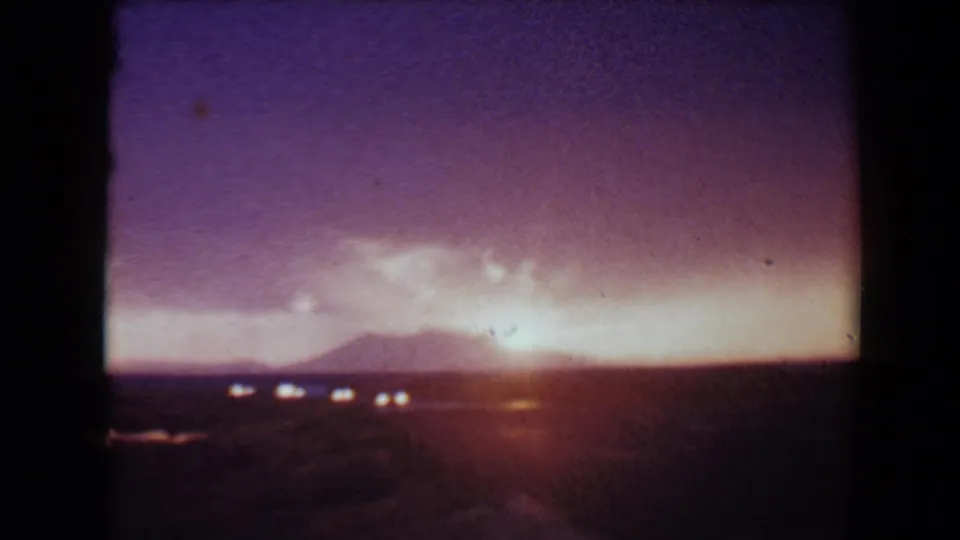1967 8mm frame near Flagstaff showing a glowing horizon, distant hills, and scattered lights across dark desert terrain.