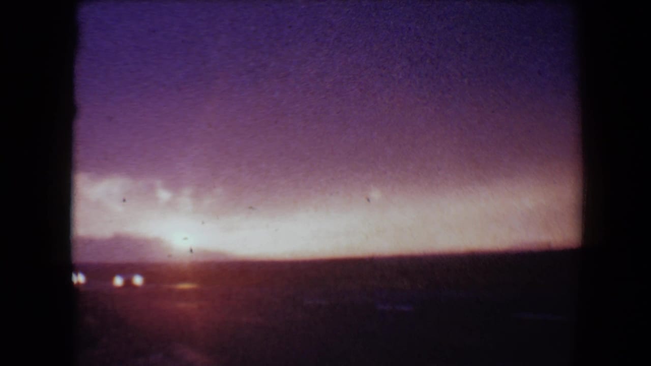 Purple and orange sunset over a dark horizon with small distant headlights.
