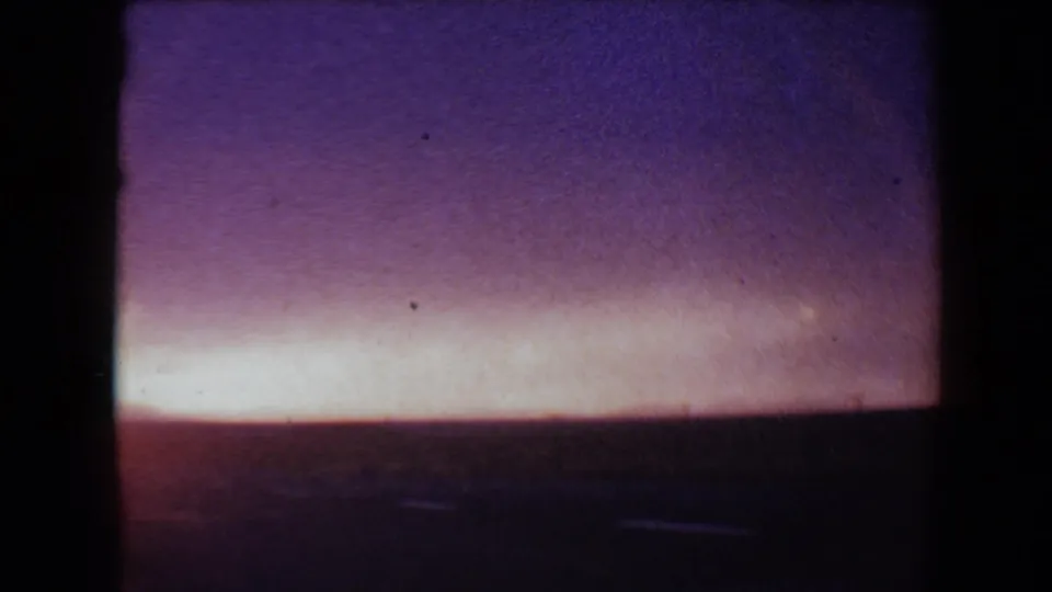 1967 Flagstaff-area 8mm frame with a low dark horizon, magenta-purple sky, and a pale orange band of fading sunset light.