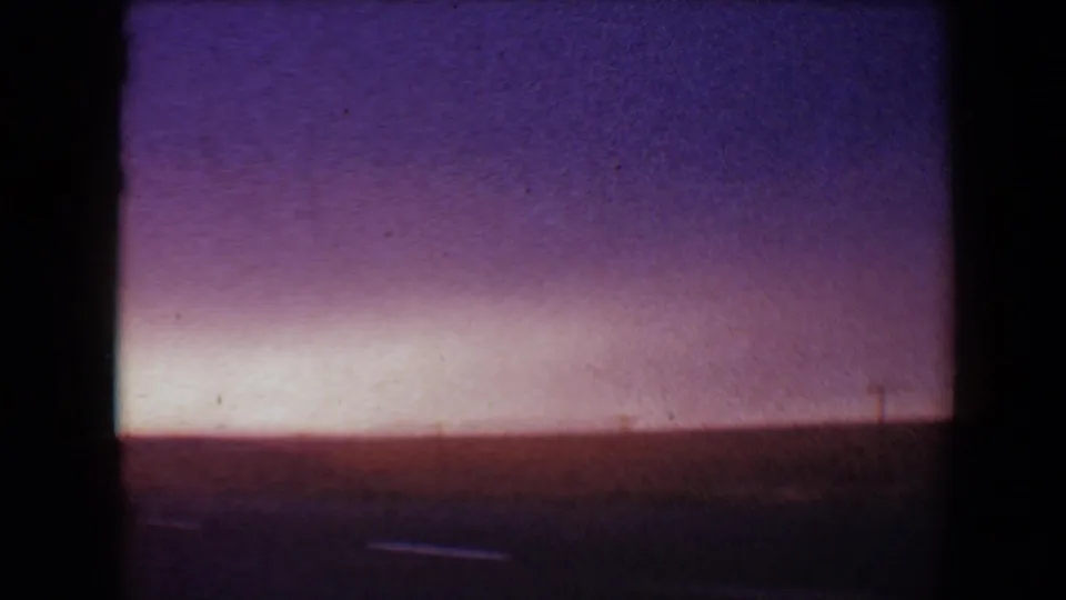 8mm home-movie frame from 1967 near Flagstaff showing soft pink-purple dusk light over a dark road or landscape foreground.