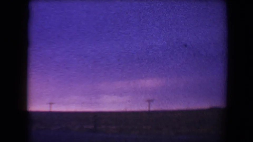 1967 8mm home-movie frame from Flagstaff, Arizona, showing a violet dusk sky above a dark roadside horizon and small utility poles.