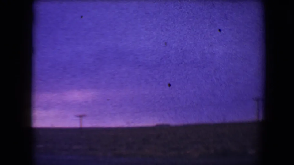 Flagstaff-area twilight landscape on 8mm film, with a broad violet sky, low dark horizon, and a distant utility pole near the frame center.