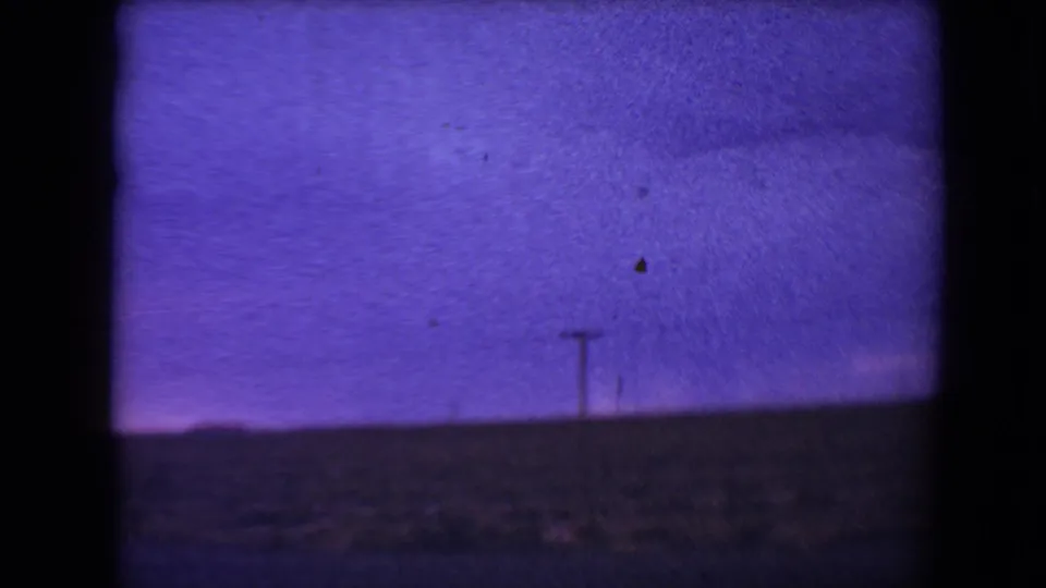 1967 Flagstaff 8mm frame showing a grainy blue-violet dusk sky, a distant utility pole, and a dark strip of roadside land.
