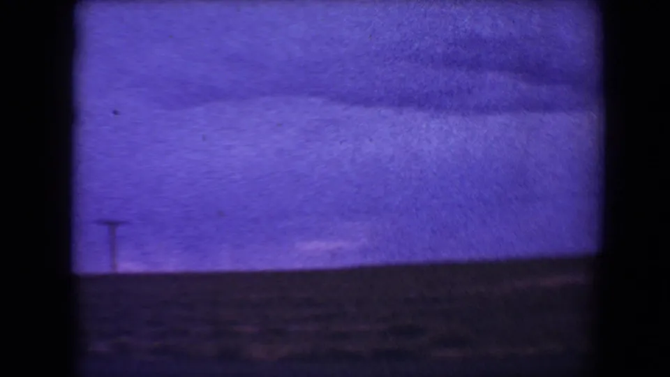 End frame of the 1967 Flagstaff home movie view, with purple twilight sky, faint clouds, dark horizon, and a small roadside utility pole.