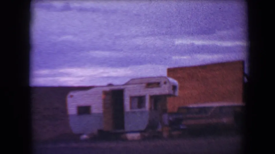 1967 Flagstaff 8mm frame with the travel trailer centered near a brick structure, the sky tinted purple by aged film color.