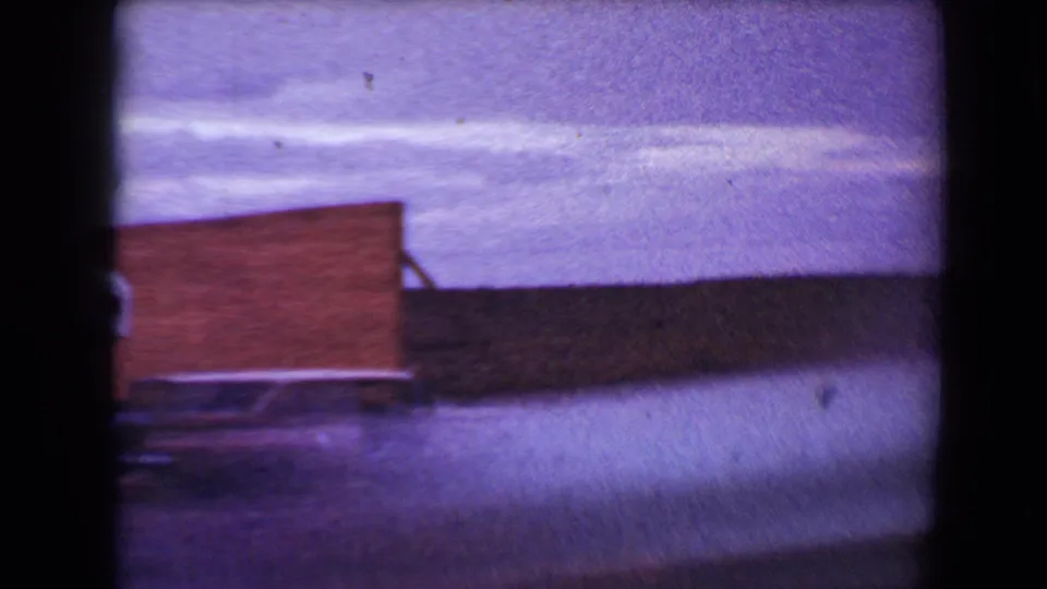 Final 1967 Flagstaff frame with the brick drive-in structure, paved foreground, cloudy sky, and the trailer mostly cropped at the left edge.