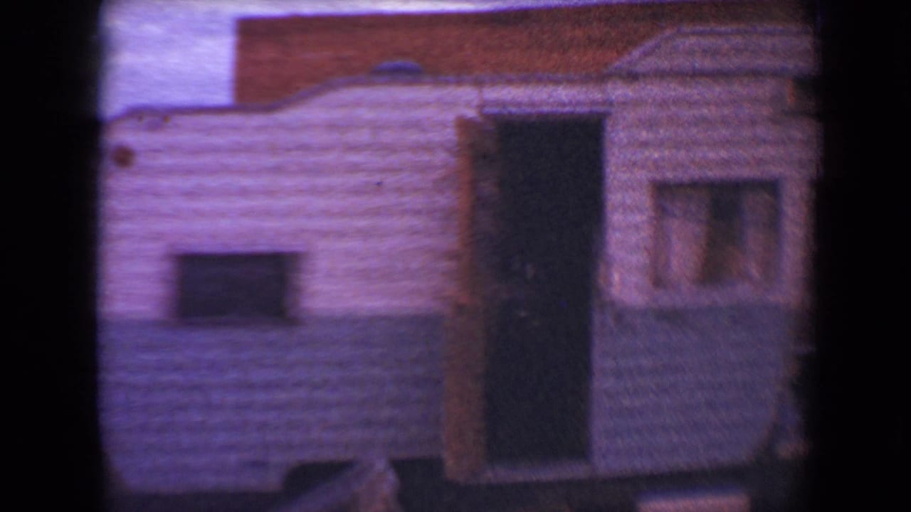 White and blue vintage travel trailer with an open dark doorway and curtained side window.