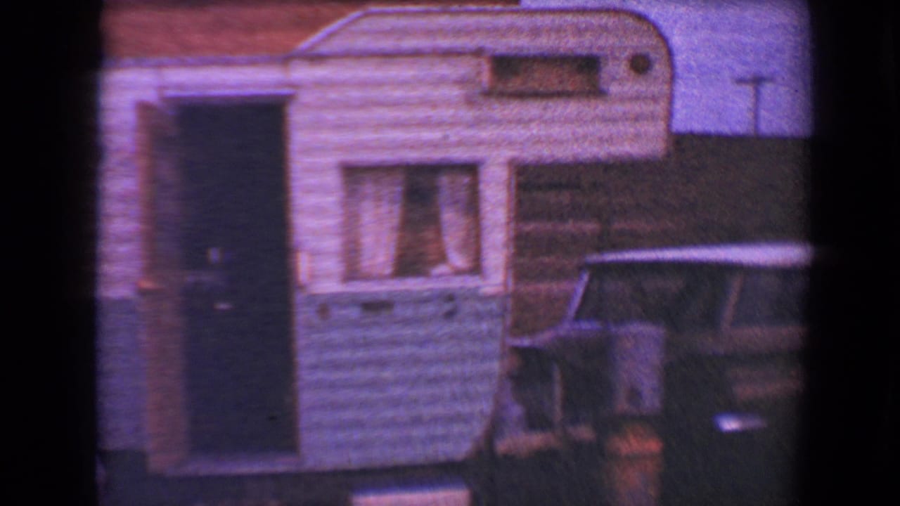 Travel trailer side with open door, curtained window, and part of a station wagon beside it.