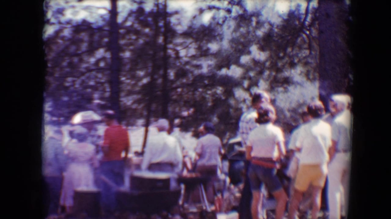 Home-movie frame of adults clustered near a smoky barbecue area during a 1967 Flagstaff gathering.