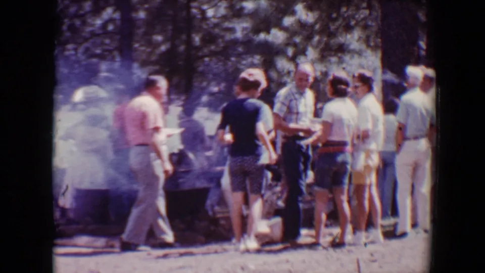 People in a wooded Flagstaff park move around a smoky barbecue serving area in 1967 footage.
