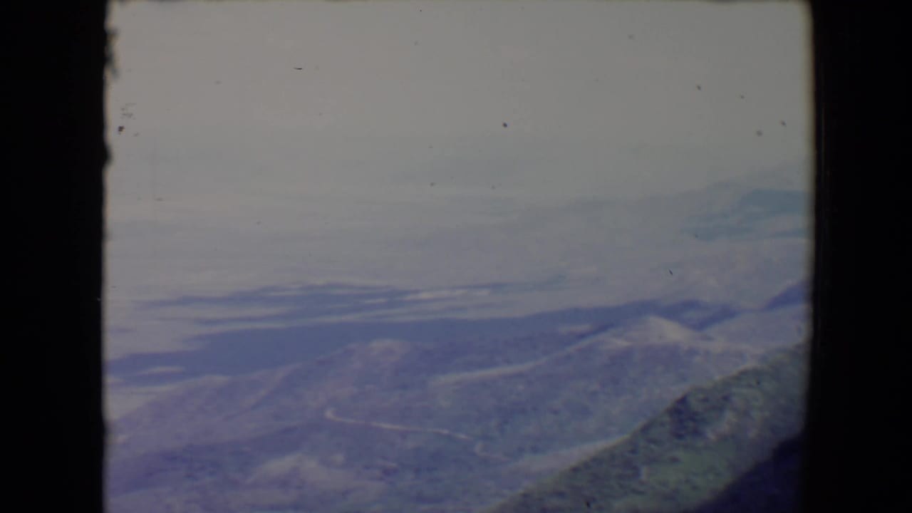 Hazy aerial view over mountain ridges with pale lakes and dark film borders.