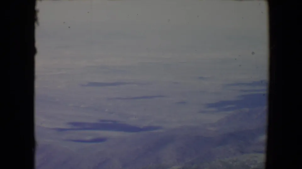 1967 8mm landscape frame near Flagstaff with low ridgelines, scattered lake surfaces, and subdued color from the film scan.