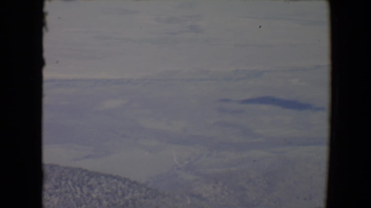 Hazy valley and distant mountains seen through dark film or window borders.
