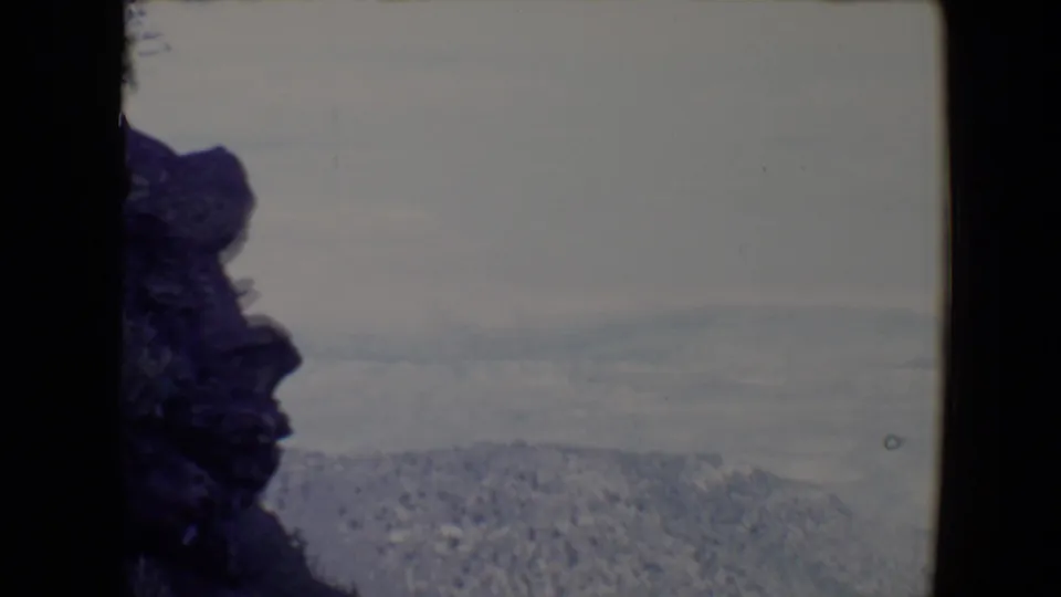 8mm view from a rocky Flagstaff overlook, showing a hazy valley beyond a forested slope and distant ridgelines.