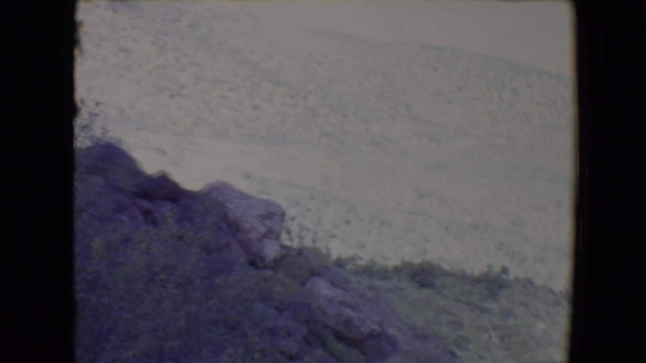 Rocky hillside beneath a bright pale sky with sparse vegetation.