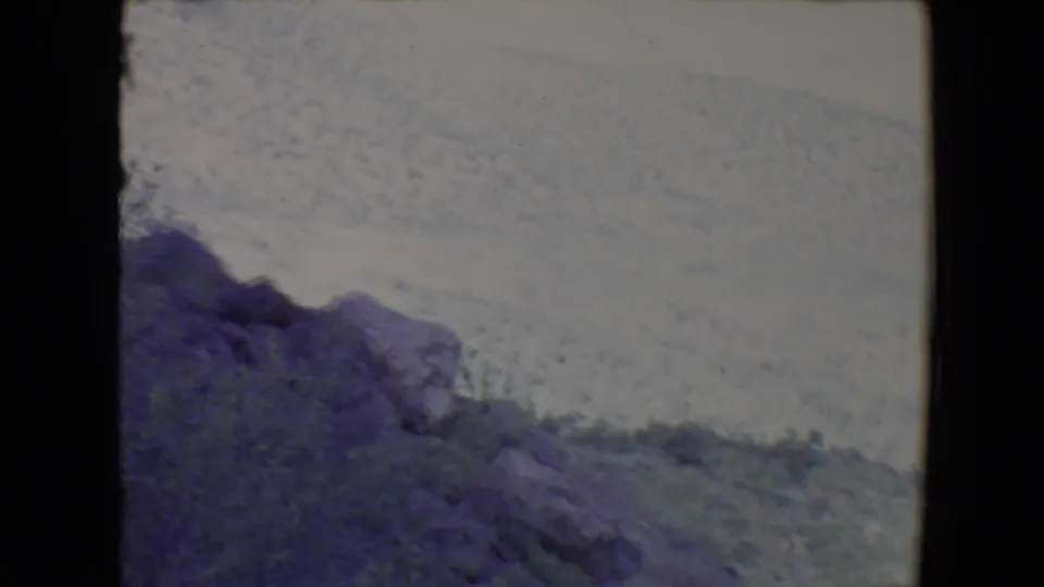 1967 Flagstaff-area 8mm frame showing a rocky, scrub-covered hillside under a washed bright sky.