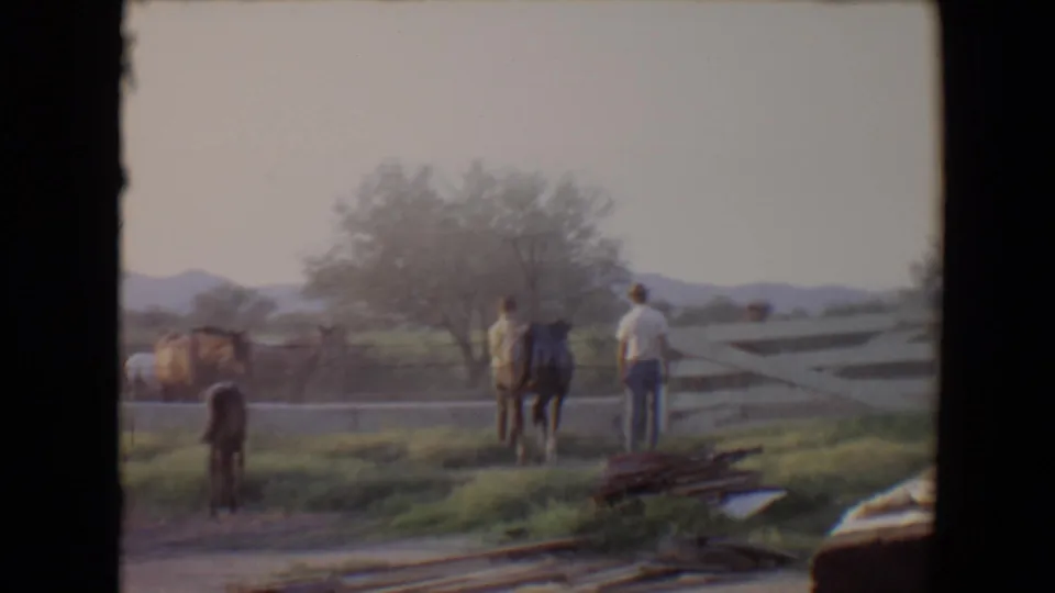 1967 Flagstaff 8mm frame showing a man and horse from behind near a farm fence, with a foal and other horses in the yard.