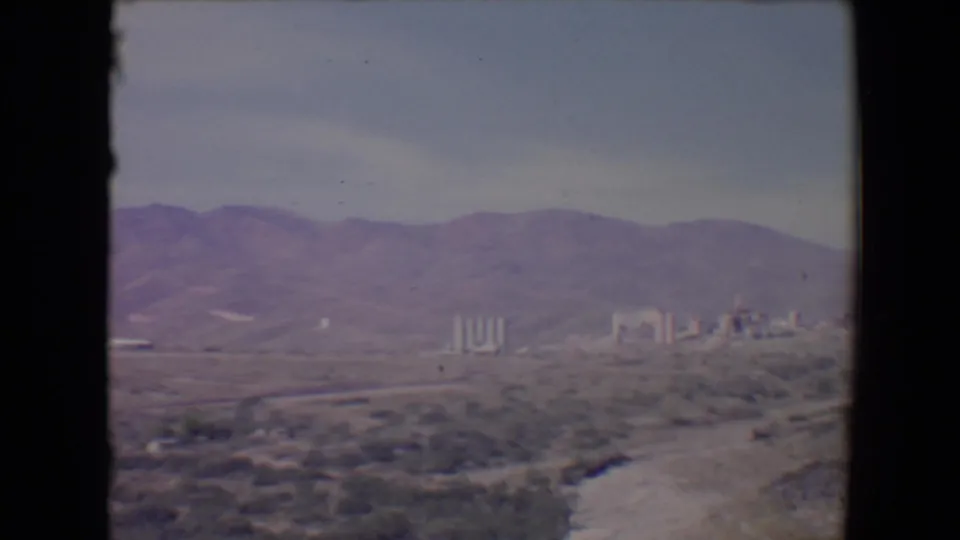1967 Flagstaff-area home-movie frame with low mountains, open scrub terrain, and small industrial structures on the horizon.
