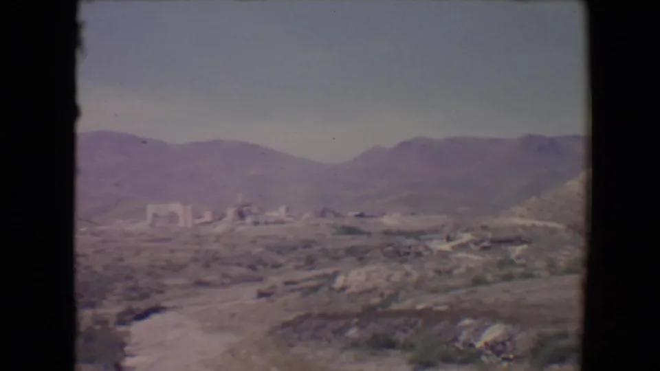 1967 8mm view near Flagstaff showing arid hills, distant low buildings, mountains, and a pale sky.