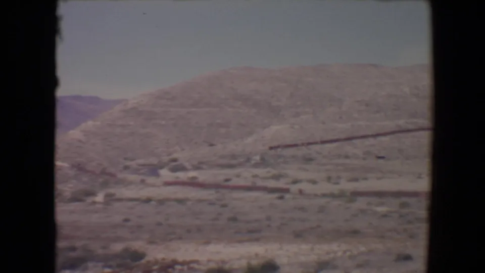 Flagstaff-area 1967 home-movie view of a dry hillside, sparse brush, pale sky, and a dark horizontal feature on the slope.