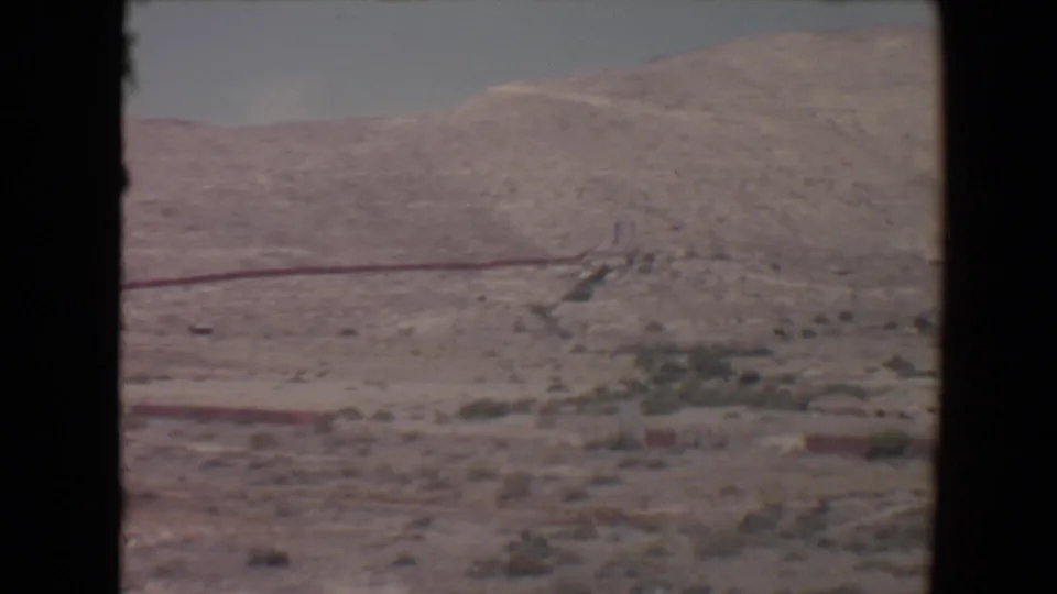 Flagstaff-area desert landscape on 8mm film, with pale hills, scattered vegetation, and a red linear feature on the slope.