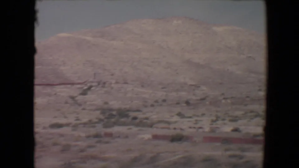 Vintage 8mm frame of a sunlit Flagstaff-area desert slope, sparse plants, and a red line near the base of the hill.