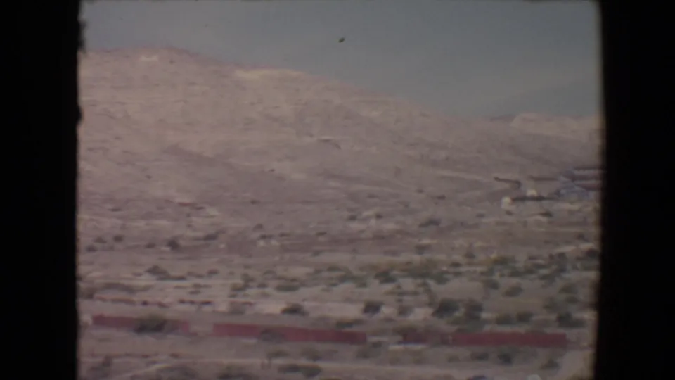 Wide 1967 8mm view near Flagstaff showing barren hills, low scrub, distant mountains, and dark borders from the film scan.