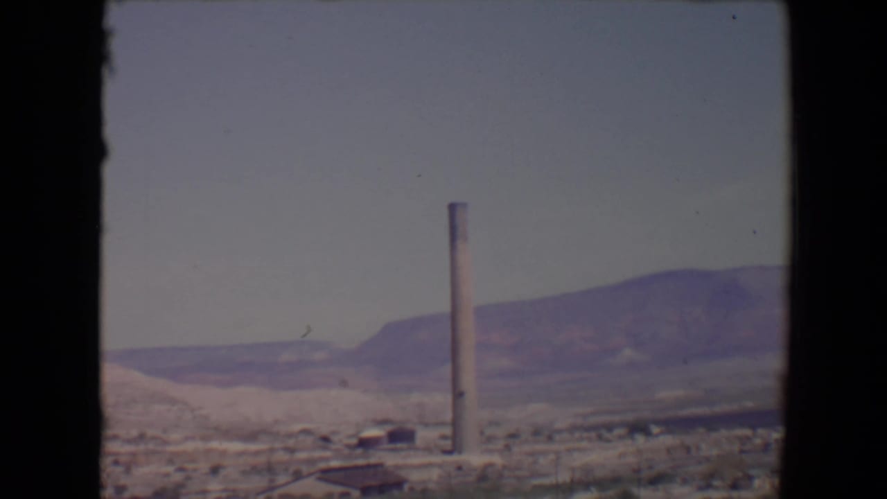 1967 Flagstaff-area valley view with a tall smokestack rising above sparse buildings and desert vegetation.