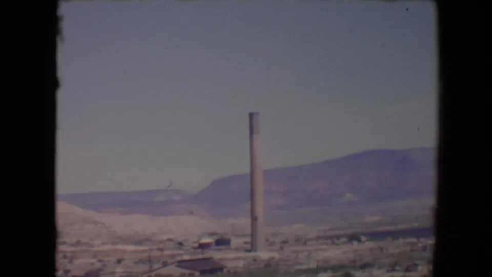 1967 Flagstaff-area valley view with a tall smokestack rising above sparse buildings and desert vegetation.