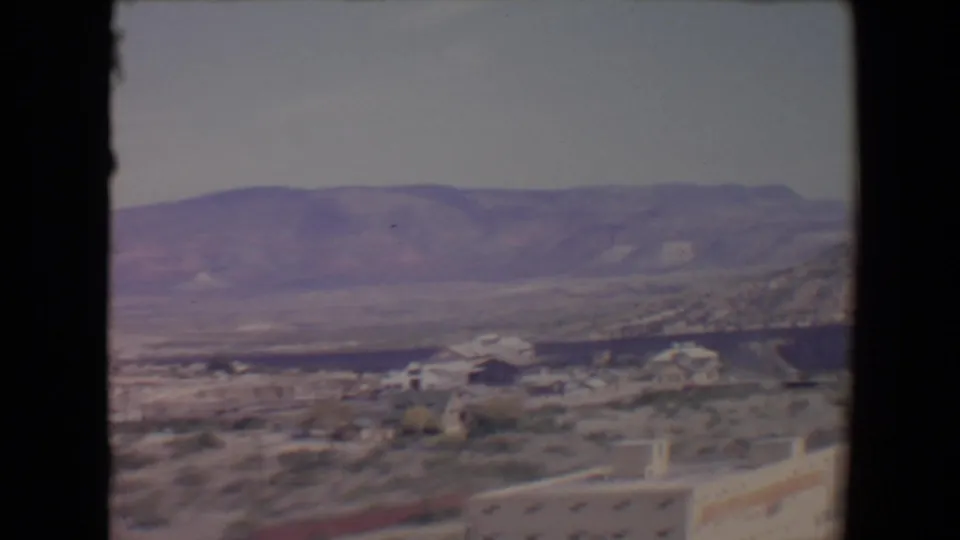 1967 Flagstaff-area view across houses, small trees, open desert ground, and a wide mountain backdrop.