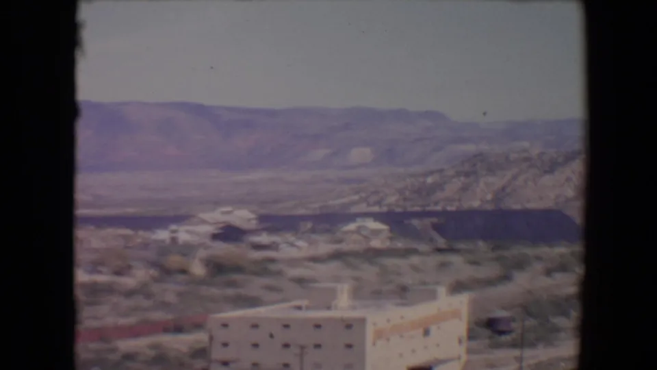 1967 Flagstaff-area desert valley view with a multi-storied building in the foreground and rugged hills beyond.