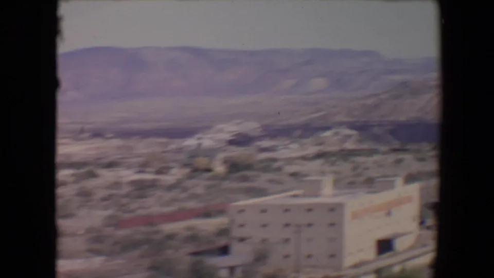 Flagstaff-area townscape on 8mm film, with a pale building in the foreground and arid mountains across the horizon.